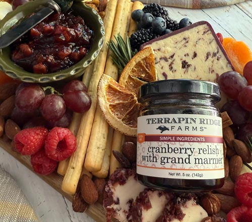 View A jar of Terrapin Ridge Farms Cranberry Relish with Grand Marnier placed on a styled charcuterie board with crackers, grapes, blackberries, dried orange slices, and cheese.